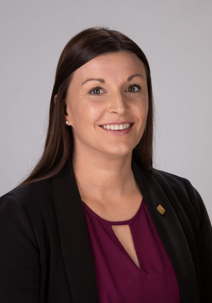 Woman with straight brown hair, wearing a blazer and maroon top, smiling at the camera.