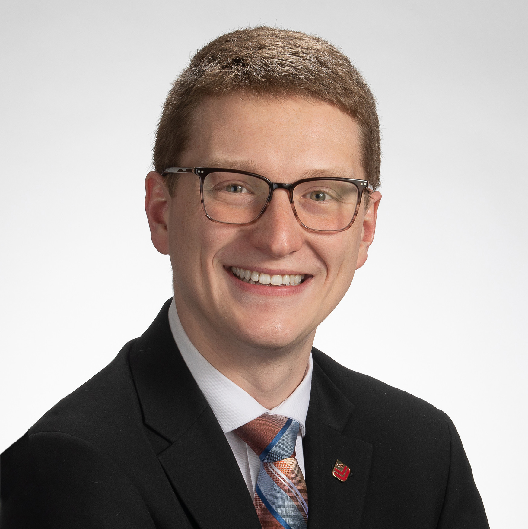 Smiling person with short hair, glasses, and suit against a plain white background.