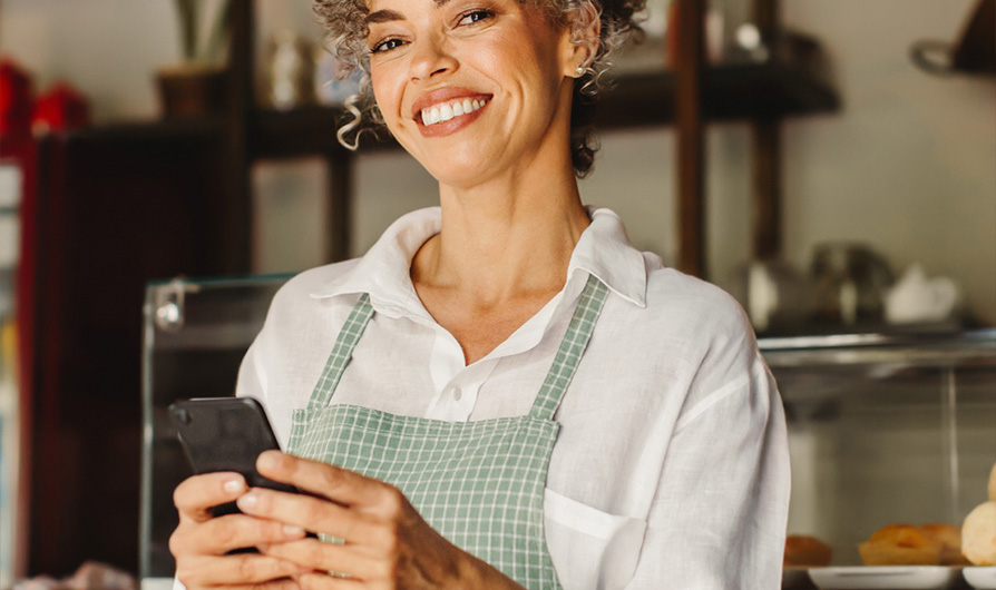 Woman smiling while holding a cell phone in a bakery.