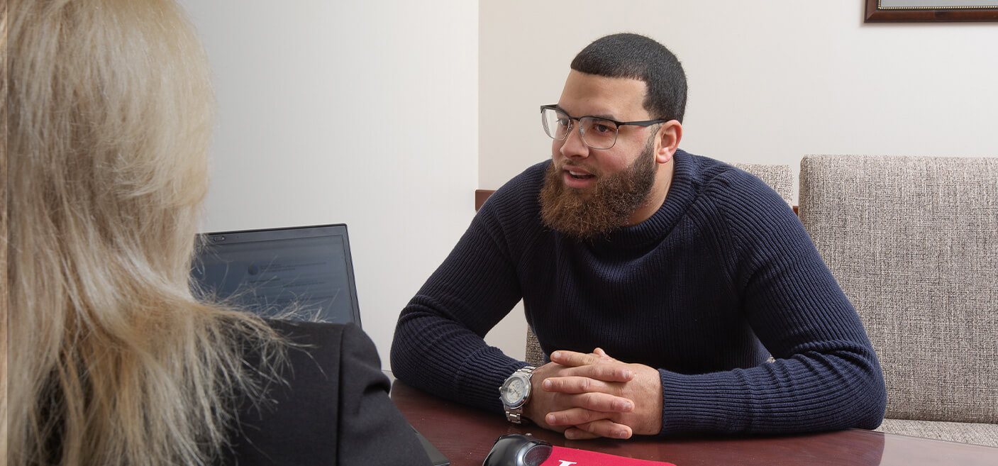 A man with glasses sitting at a desk, using a laptop and holding a credit card.