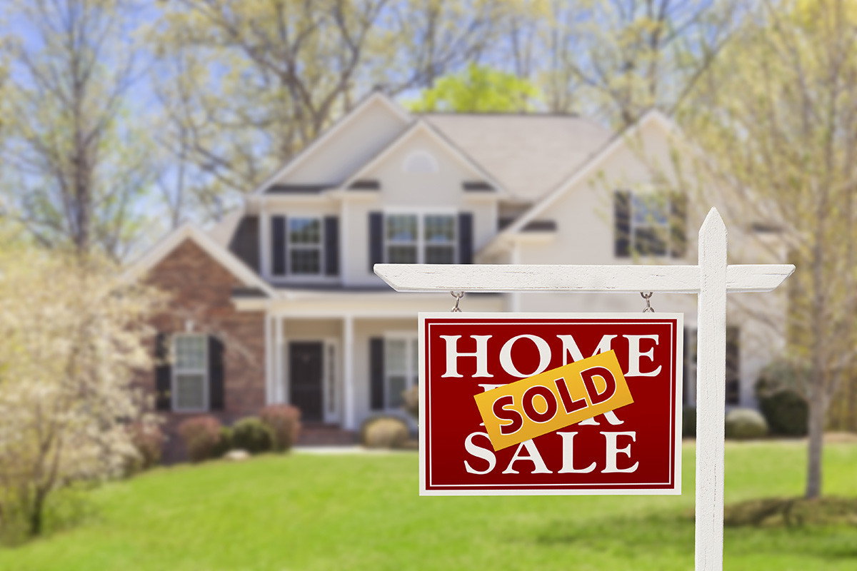 A Home For Sale sign with a Sold sticker in front of a suburban house.