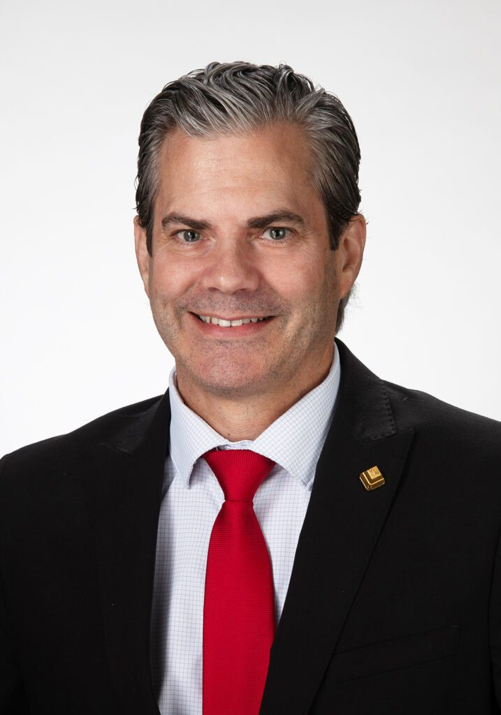 Smiling man in a suit and red tie, posing against a plain white background.