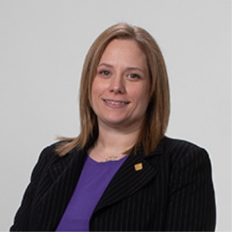 Woman with straight, light brown hair wearing a dark blazer and purple top, smiling.