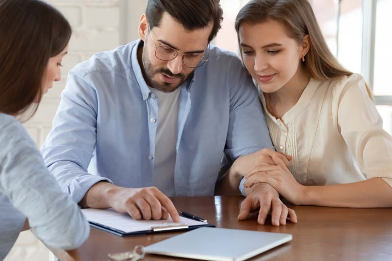 A man and woman sitting at a table with a laptop and papers, discussing work together