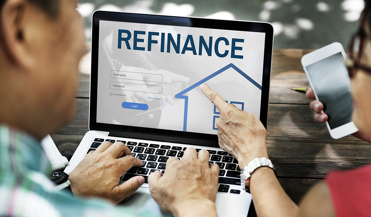 Two people view a laptop screen displaying a refinance login page with a house graphic.