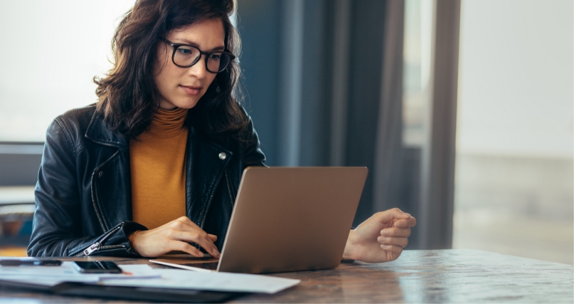 A woman with glasses working on a laptop at a table.