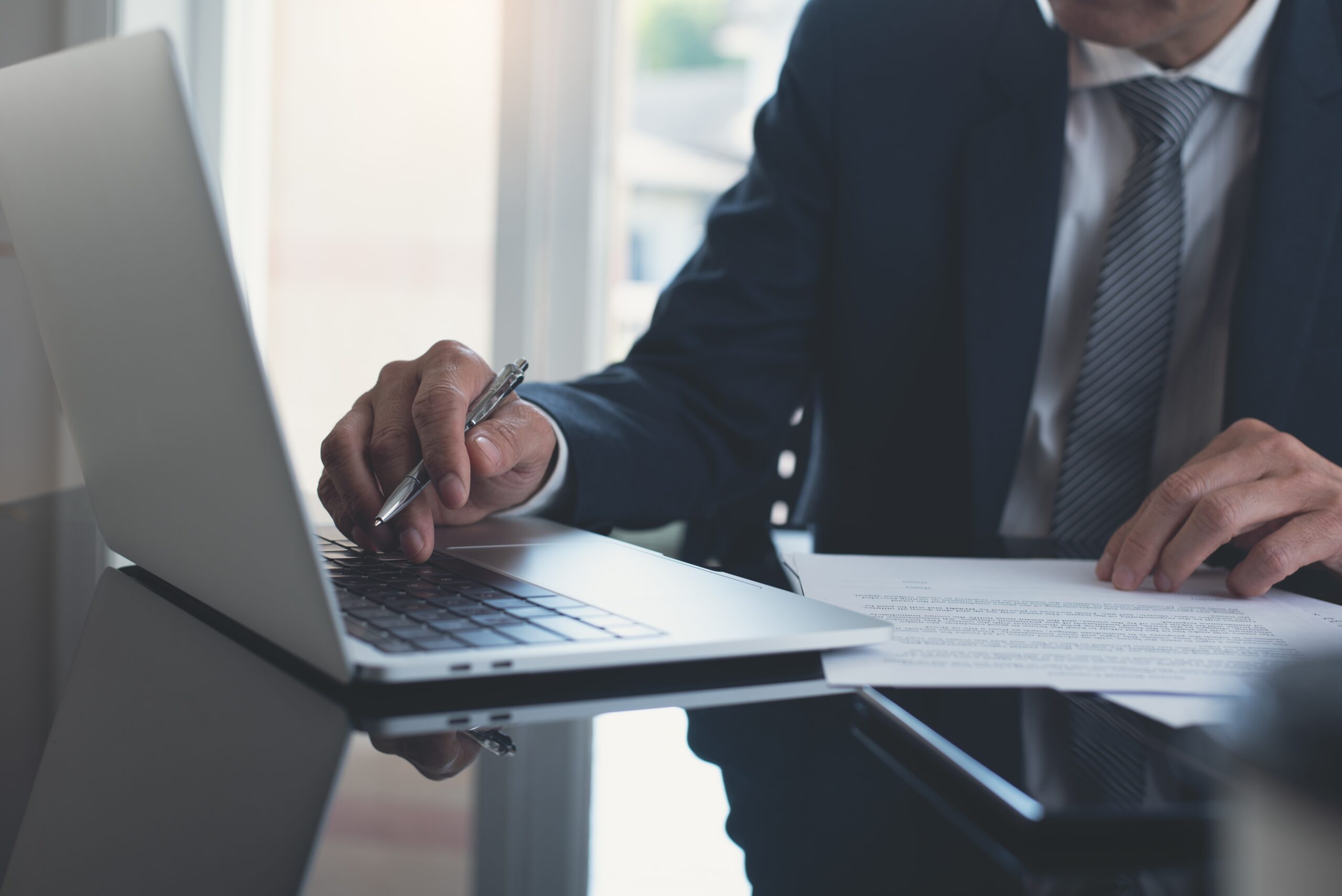 A man in a suit focused on his laptop screen, typing diligently.