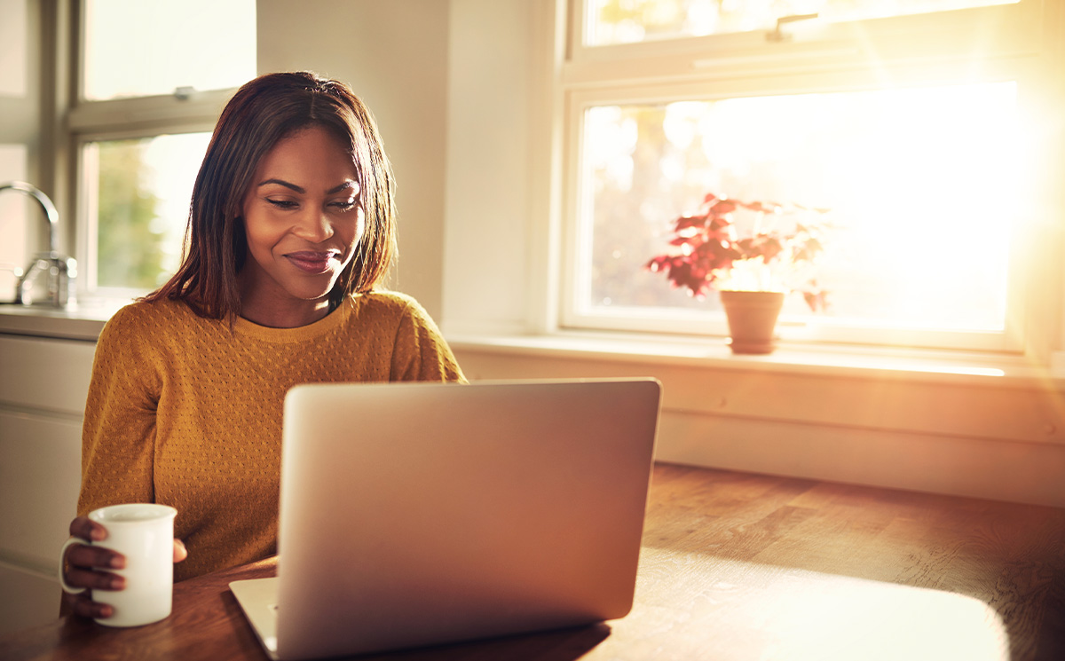 Woman sitting at table with laptop and coffee cup, working on computer.