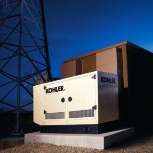 Large Kohler generator outdoors beside a utility structure at dusk, under a transmission tower.