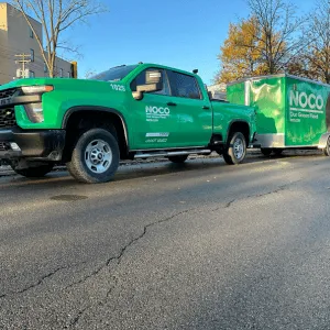A green NOCO pickup truck with a matching trailer parked on a street in daylight.