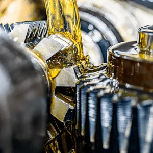 Close-up of oil being poured onto shiny metal gears in a mechanical system.