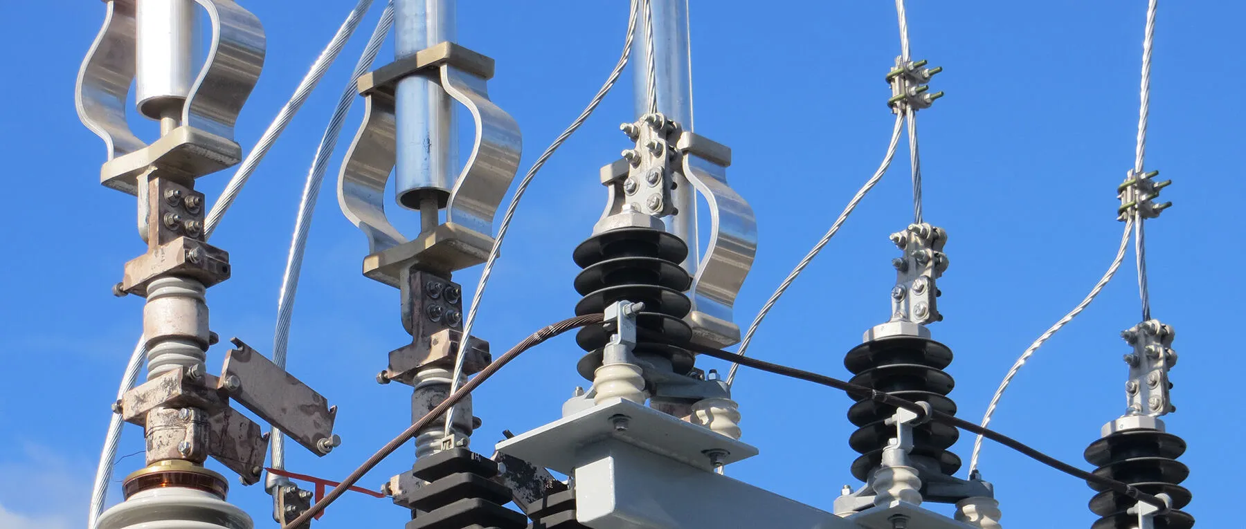 Close-up of electrical power lines and insulators against a clear blue sky.