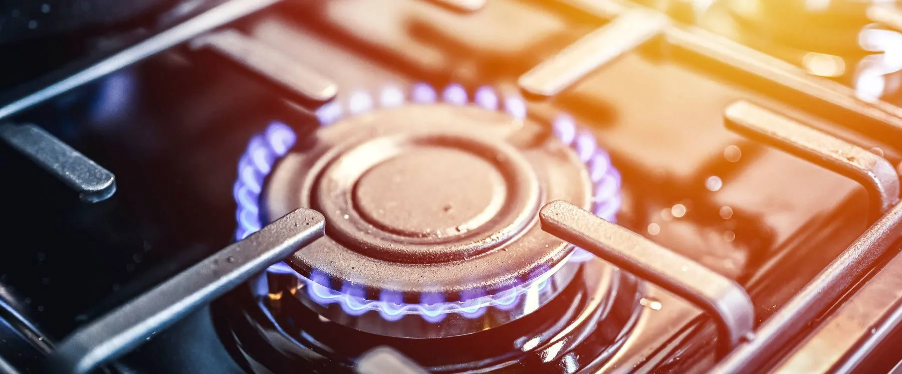 A close-up of a lit gas stove burner with blue flames and metal grates.