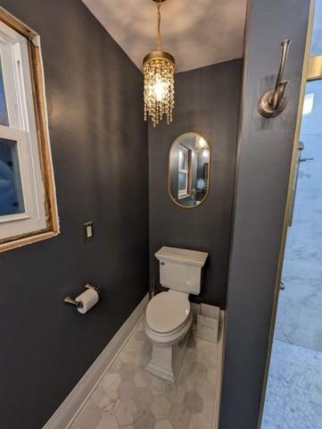 updated bathroom with light tile floors dark blye walls hold accents and gold chandiler above toilet
