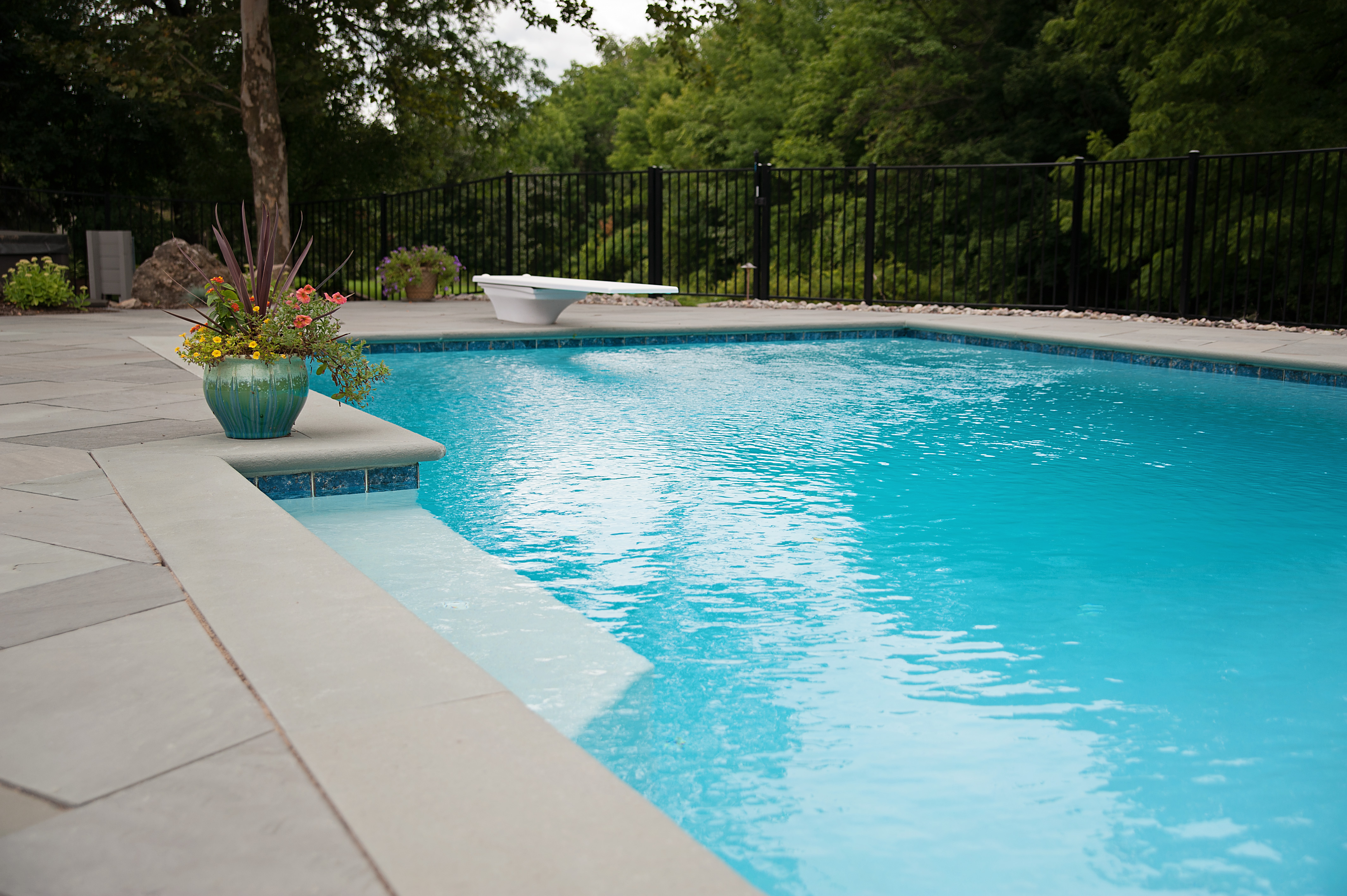 serene pool with diving board and angled concrete pool deck