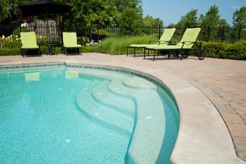 far shot of steps into pool with green lawn chairs