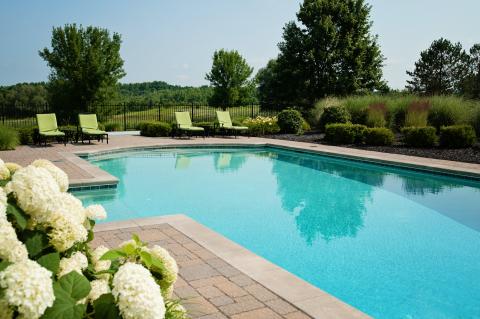 far angle image of a aqua blue pool with green lawn chairs and flowers
