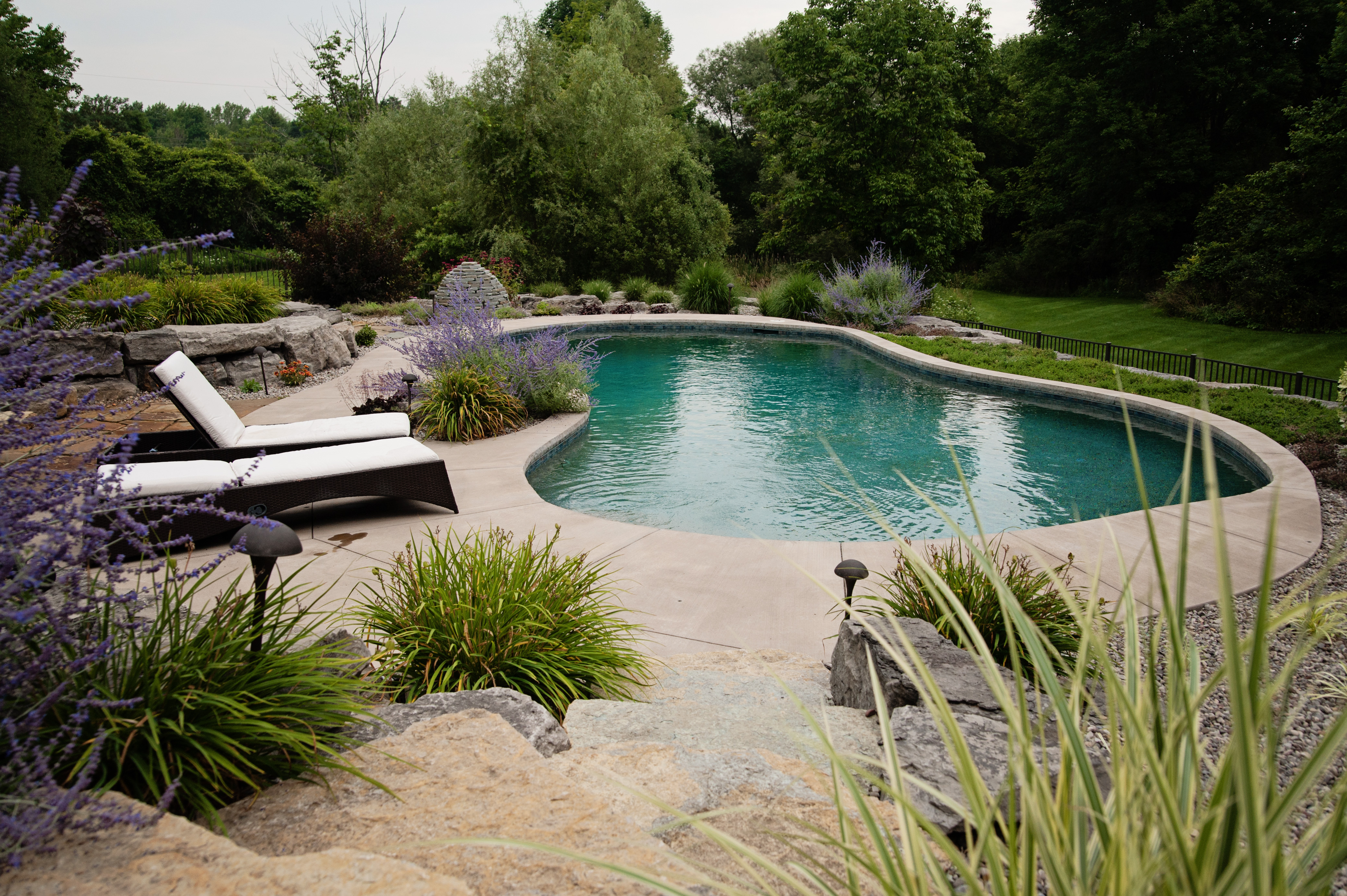 calm teal kidney shaped pool with stone landscaoping and two lounge chairs