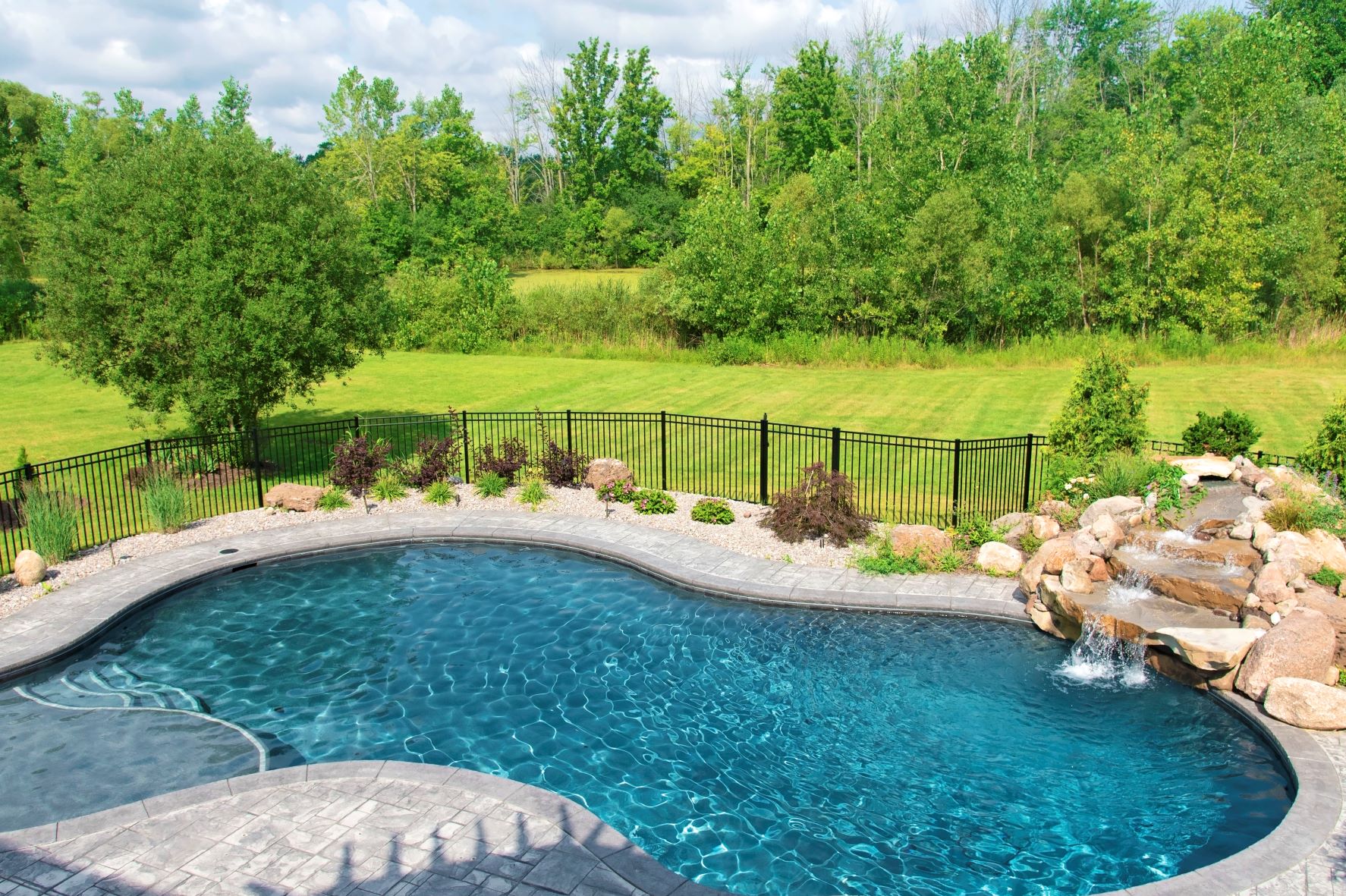 backyard pool with stone waterfall and black fence