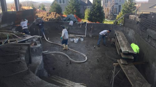 Several workers are constructing an in-ground swimming pool in a residential backyard.