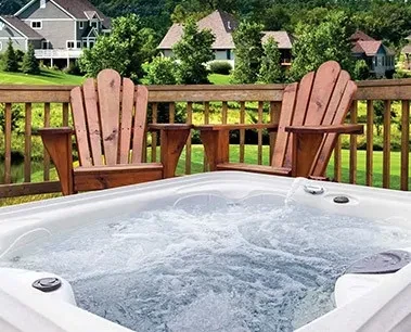 Bubbling hot tub on a deck with two wooden chairs, trees, and houses in the background.