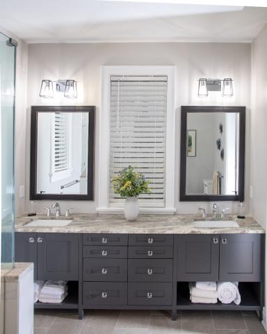 brought double sink bathroom with dark gray-brown cabinets and tan with marbled countertops