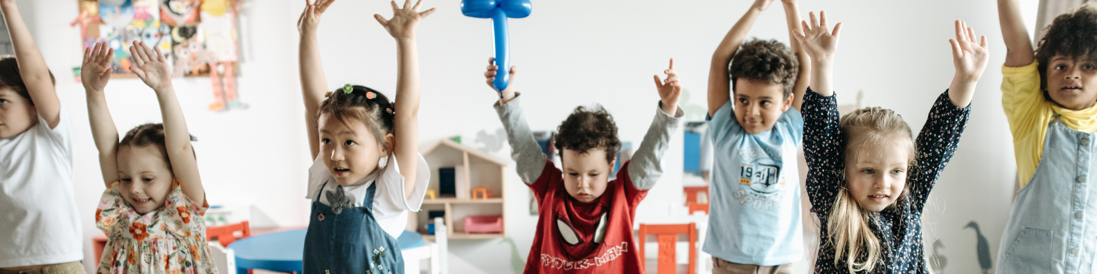 A classroom of children raising both of their hands