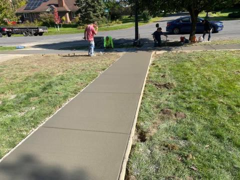 Freshly poured concrete sidewalk with people working and sitting nearby on a sunny day.