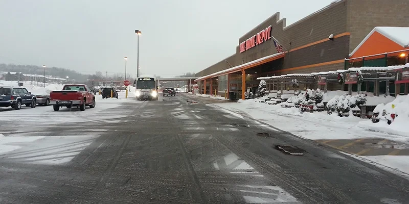 Snowy parking lot outside a Home Depot store with cars and slushy tire tracks on the ground.