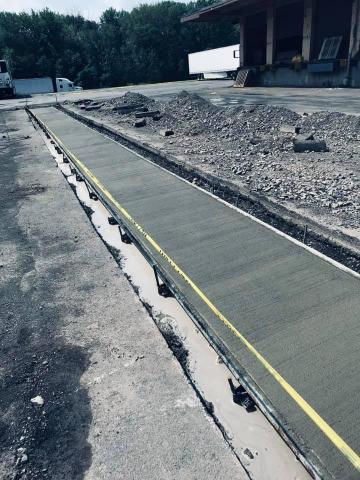 Freshly poured concrete sidewalk near a building, roped off with caution tape, curing.
