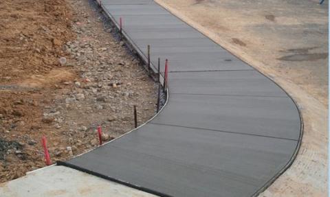 Freshly poured concrete sidewalk curves through a construction area with dirt on both sides.