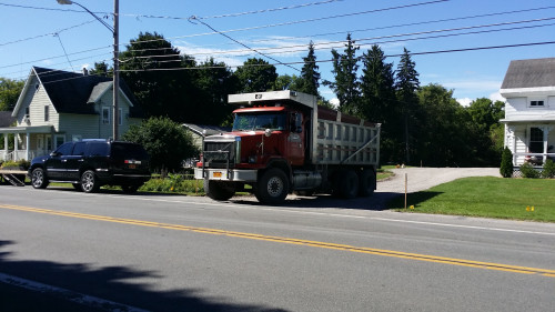 A red dump truck and a black SUV are parked on a driveway beside two houses on a sunny day.