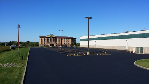 Nearly empty parking lot next to a large building, with a hotel in the background under a clear sky.