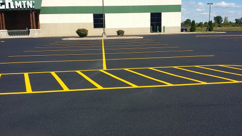 An empty parking lot with fresh yellow lines in front of a beige and green building.