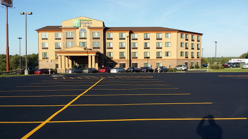 Four-story Holiday Inn Express hotel with an empty parking lot and a clear, sunny sky.