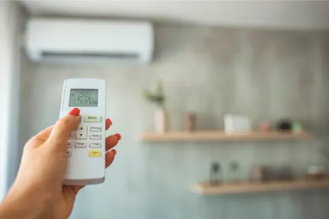 Hand holding remote control, setting temperature on air conditioner in a modern living room.