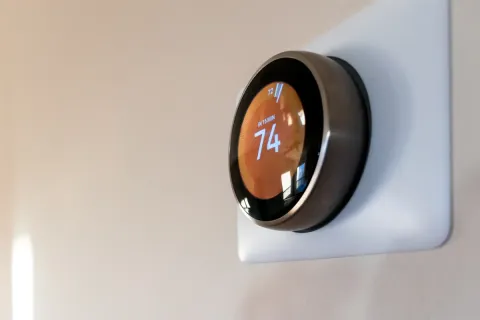 A smart thermostat on a wall displays the temperature set to 74 degrees.