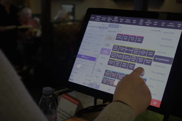 A person uses a touchscreen POS system at a restaurant.