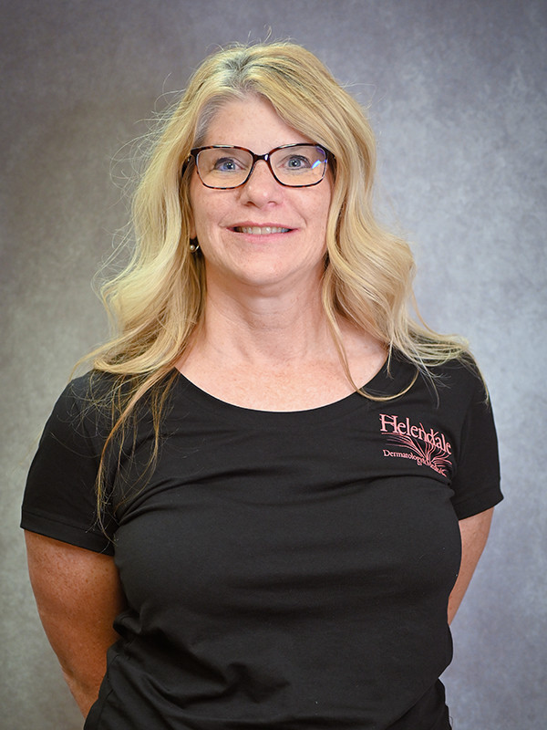 SmilinJennifer Little, Hair Center Coordinator at Helendale Dermatology wearing a black shirt, standing against a gray background.