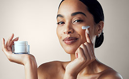 beautiful woman holding facial cream in one hand and applying it to her face with the other hand