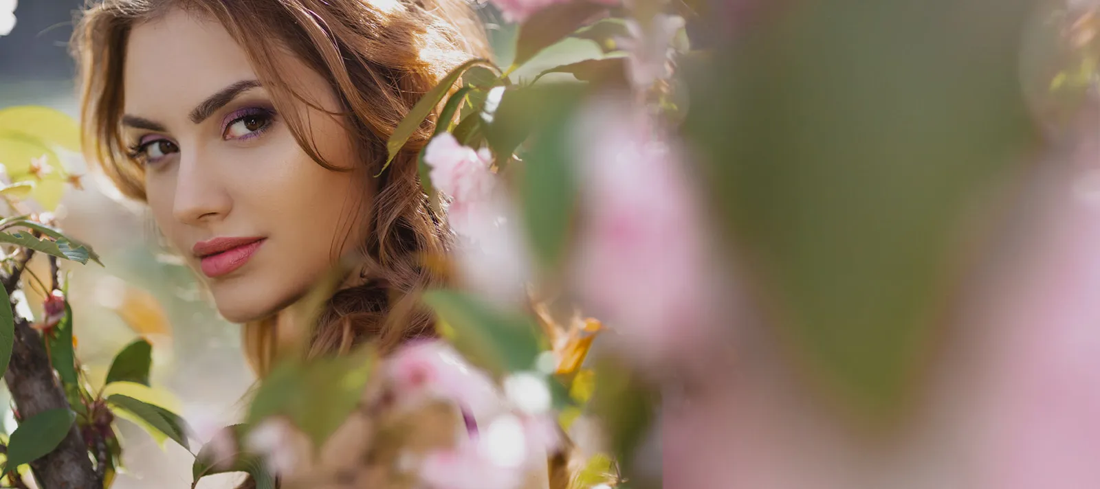 female model looking out from behind pink flower bushes