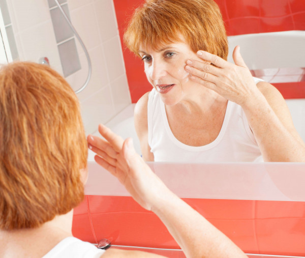 red haired woman inspecting her cheeks for rosacea in the bathroom mirror