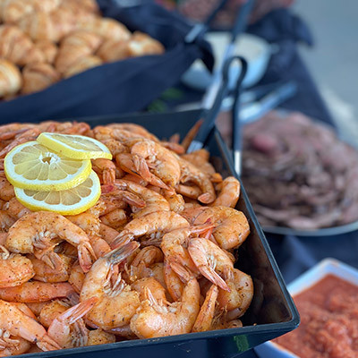 tray of seasoned shrimp garnished with lemon slices, with more seafood dishes in the background