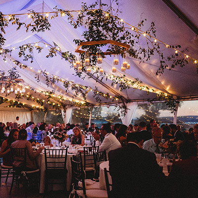 outdoor evening wedding reception under a decorated tent with guests seated at round tables