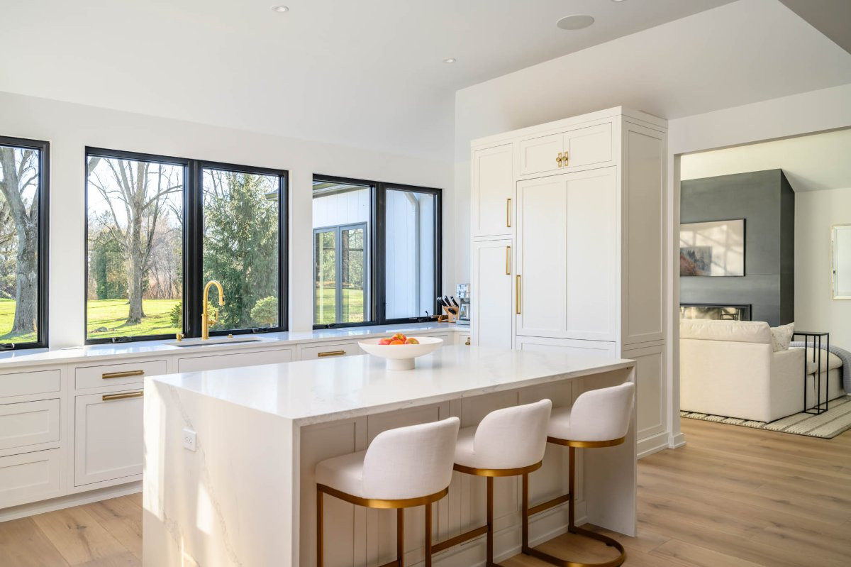Bright modern kitchen with white cabinets, island seating, and large windows overlooking a yard.