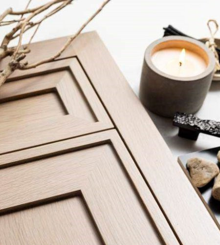 Light wood cabinet doors beside a lit candle, sticks, and stones on a white surface.
