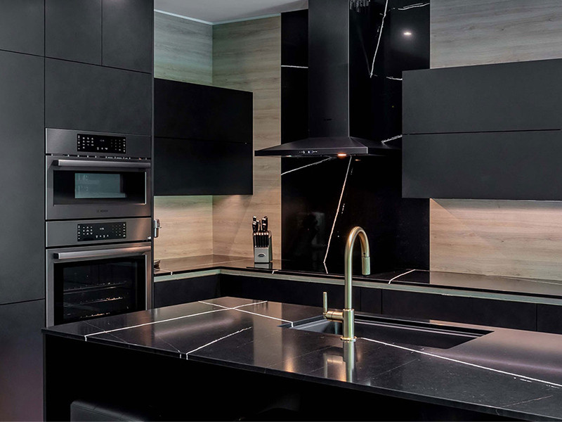 Modern kitchen with black cabinets, marble countertops, a gold faucet, and built-in appliances.