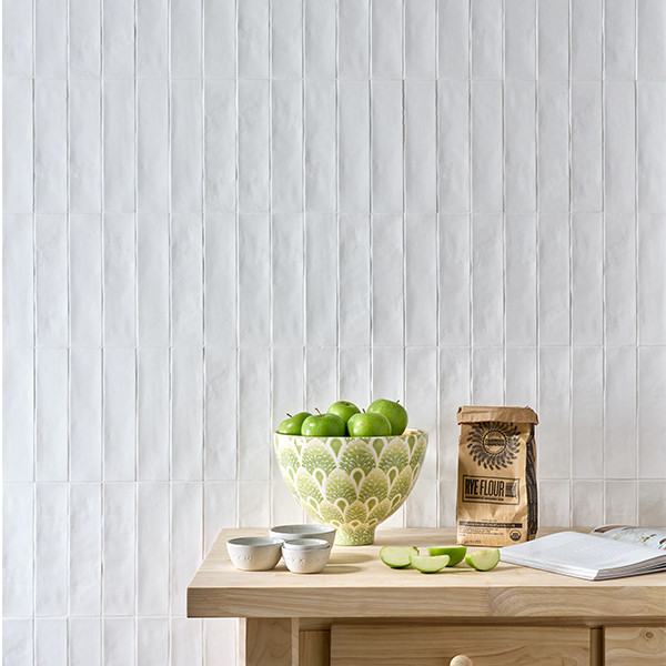 A bowl of green apples, rye flour, cups, and sliced apples on a wooden table against a white tile wall.