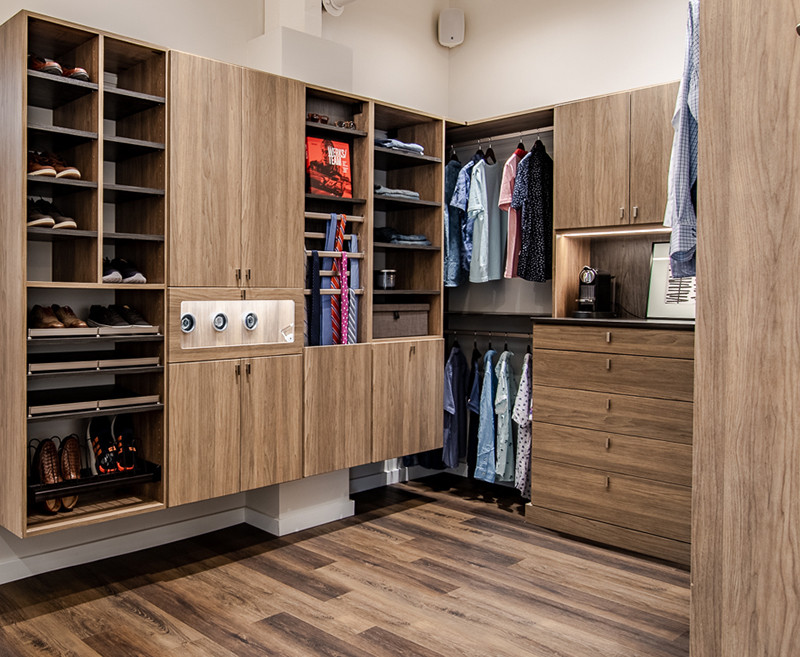 Modern walk-in closet with wooden cabinets, shelves, hanging clothes, and organized shoes.