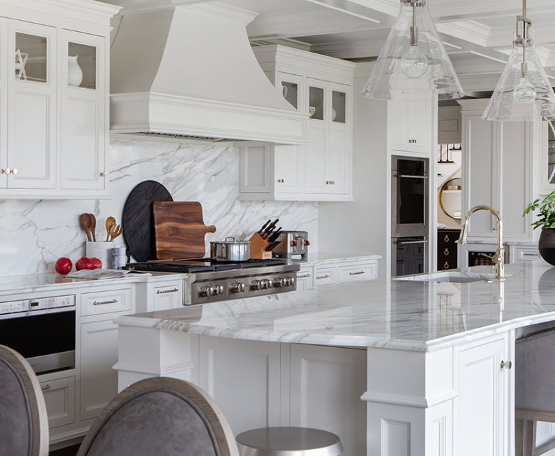 Modern white kitchen with marble countertops, island, and stainless steel appliances.